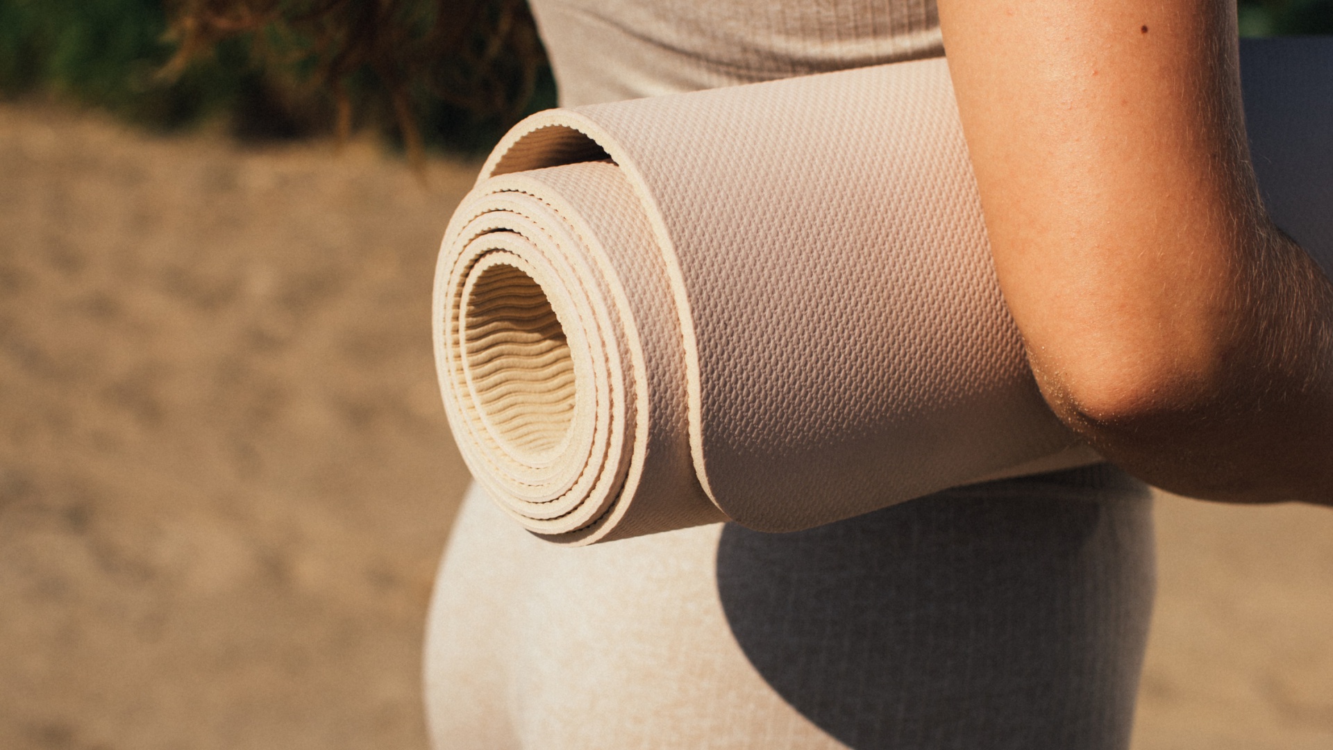 Frau mit aufgerollter Pilatesmatte unter dem Arm