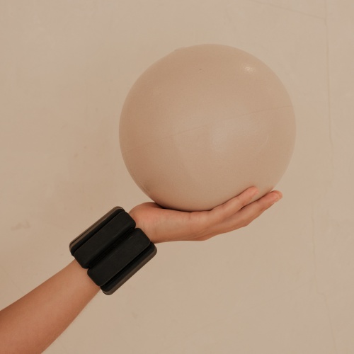 Hand mit Gewichtsmanschette hält einen Pilatesball